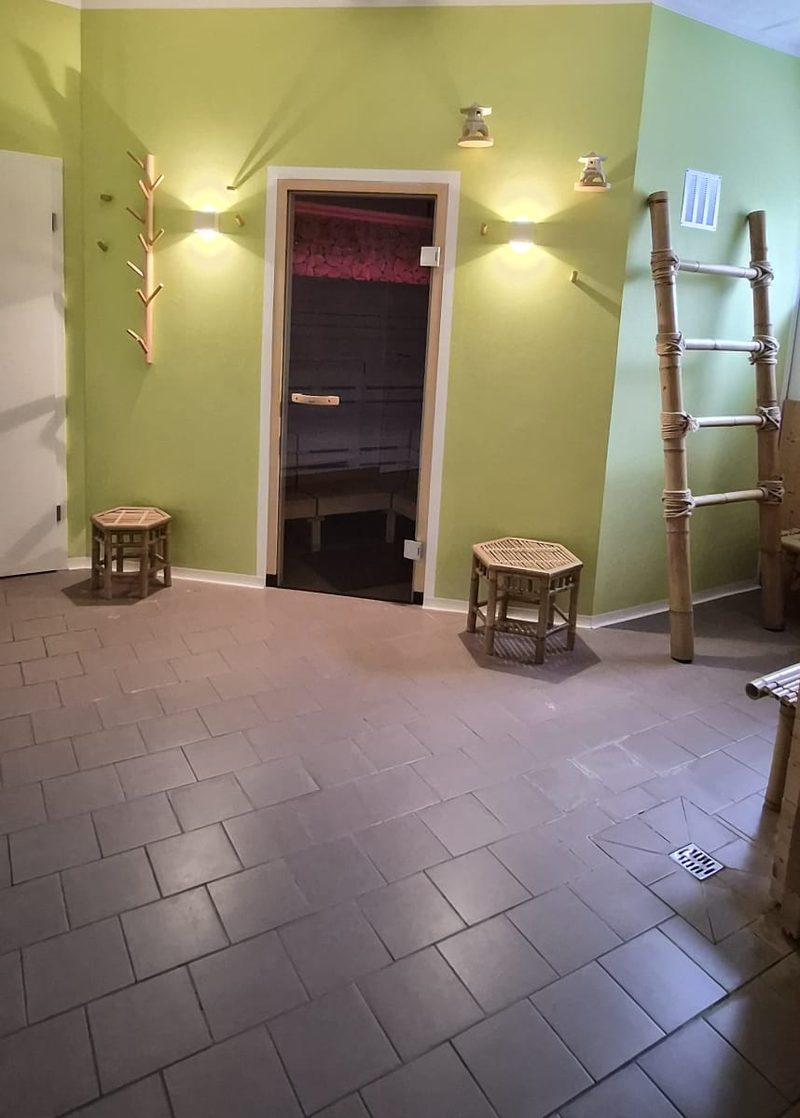 Saunabereich mit grüner Wand und Glastür zur Sauna